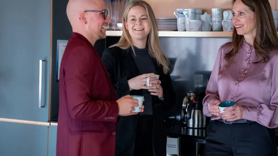 Tre blide ansatte ved kaffemaskin
