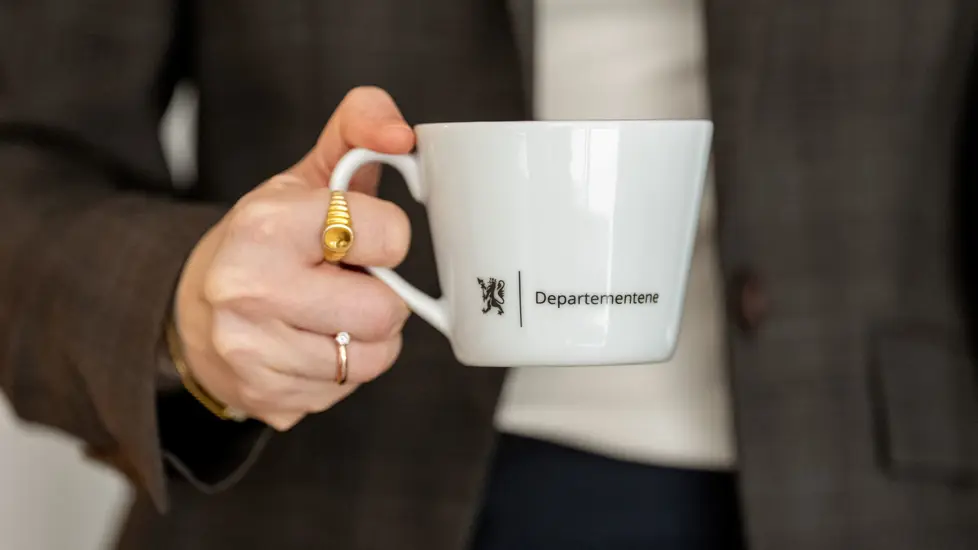 En dame som holder en hvit kopp med Departementene på