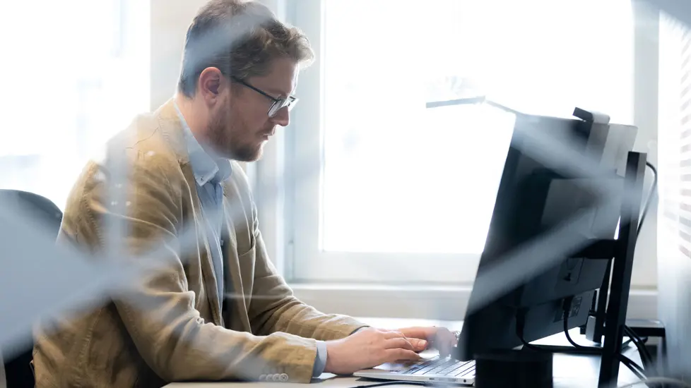 Mann sitter og jobber ved PC.