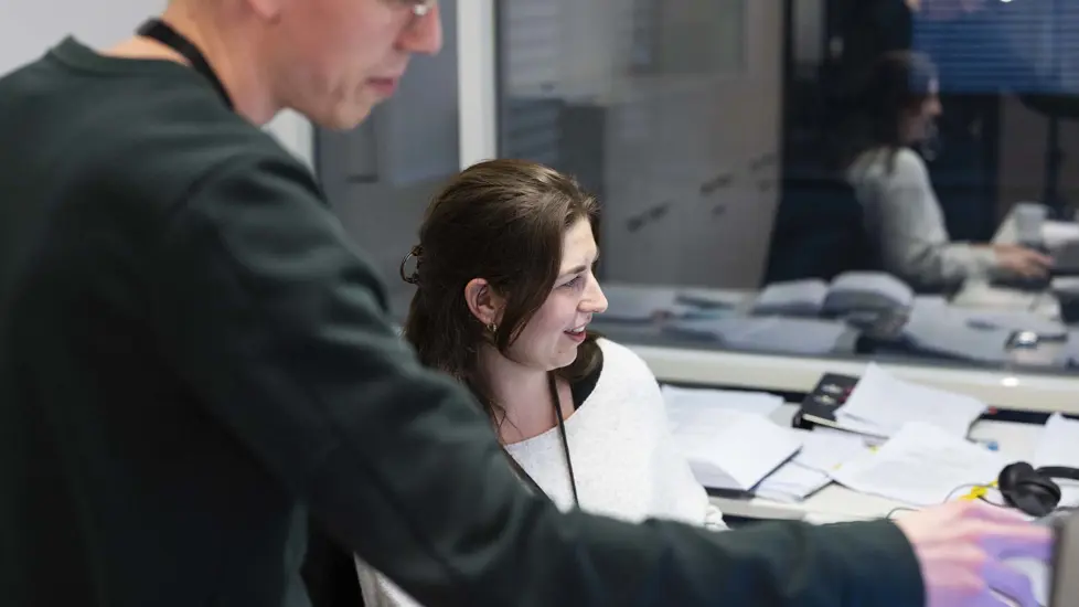 Kvinnelig ansatt sittende ved pc, mannlig ansatt stående ved siden av som peker mot skjermen