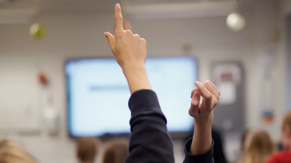 Elever som rekker opp hendene i et klasserom